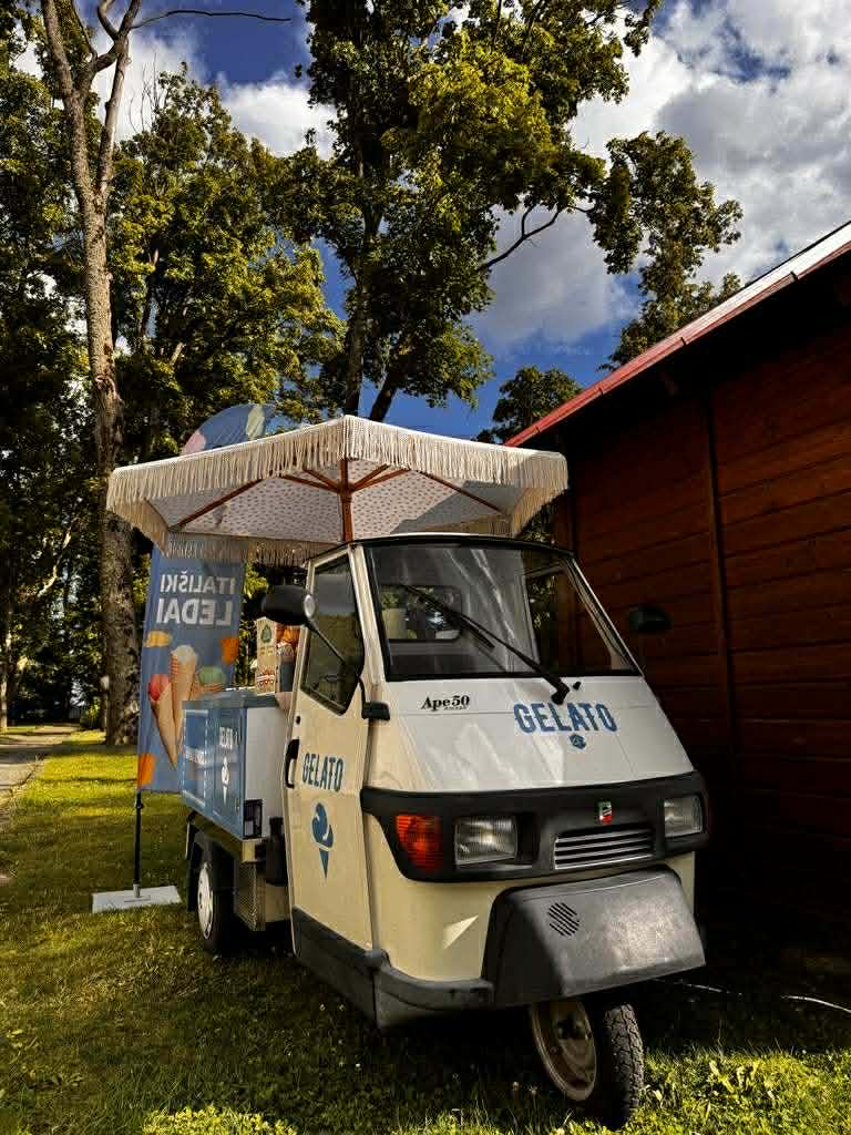 Piaggio Ape 50 gelato truck at outdoor event with Italian ice cream banner